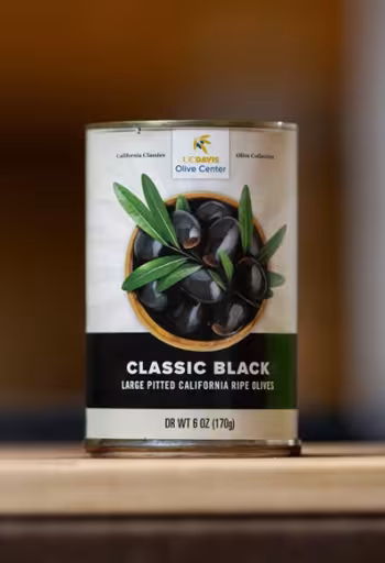 Can of "Classic Black" olives with illustrated olive sprig on wooden table