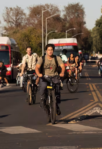 Commuters cycling on a sunlit city street with buses behind