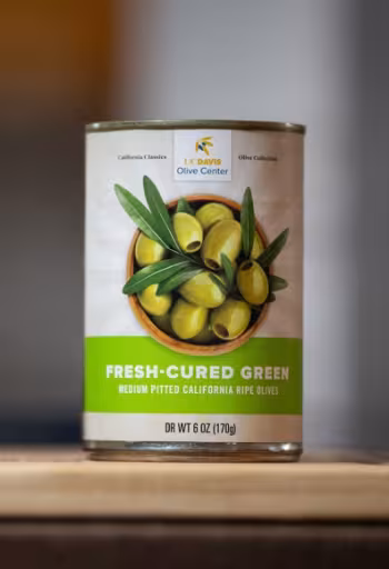 Can of fresh-cured green olives on wooden surface with blurred background