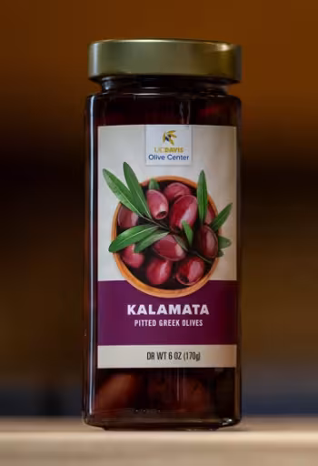 Glass jar of Kalamata olives with illustrated label and gold lid, on wooden surface