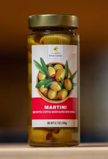 Jar of Martini green olives on wooden surface with warm blurred background