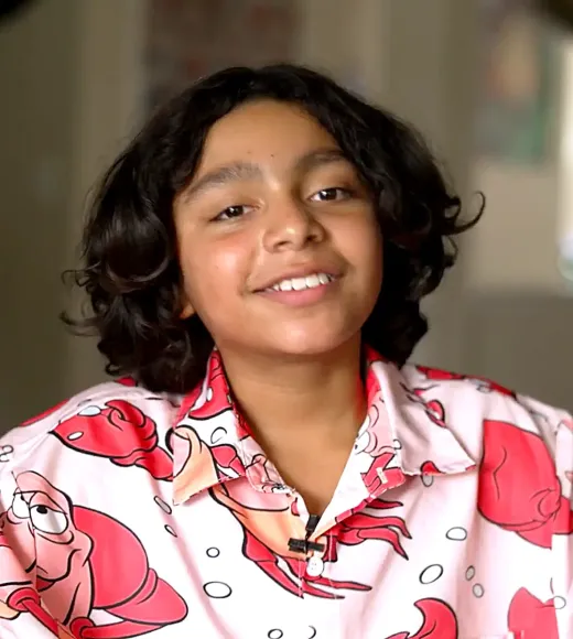 A smiling child with curly hair wearing a colorful crab-themed shirt.