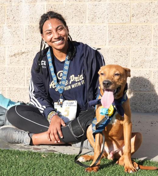 Runner sitting, wearing medal, next to dog with tongue out