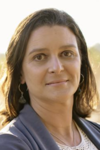 Outdoor portrait photograph of a woman with shoulder-length brown hair, neutral expression