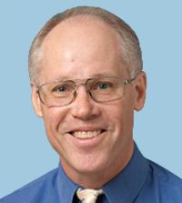 Smiling man with glasses in blue shirt against light blue background