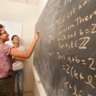 A student writes equations on a chalkboard covered with math. 