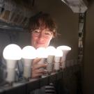 A smiling student screws on a row of bright light bulbs.