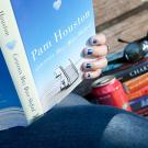 Woman reading a book by Pam Houston on a bench with other books, a can of pop and sunglasses