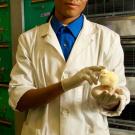 Matthew Warren in a lab coat and gloves holding a chick.