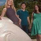 Two female students and a male posing in front of an Egghead sculpture