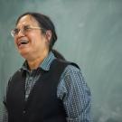 Male professor laughs in front of blackboard