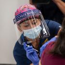 Nurse in face shield and mask, administers a vaccination.