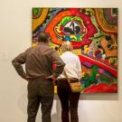 Two people viewing a framed work of art on wall.