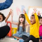 Children excitedly throw up their hands in child care.