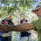 Dave Rizzo points at tree, in field class with students