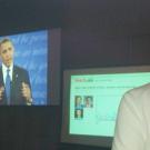Obama on video screen next to a monitor showing new app being watched by a man with his back to the camera