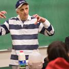 Photo: Ed DePeters gesturing in front of a blackboard with students listening. Bottles of milk and chocolate milk are on the desk.