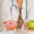 Doctor has doughnut in one hand, apple in the other.