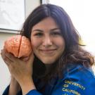 Female student  in UC Davis blue lab coat holds model of brain close to her smiling face.