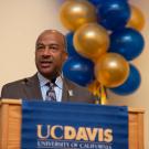 Chancellor Gary S. May at podium with blue and gold balloons in background.