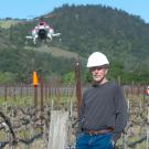 Professor D. Ken Giles in vineyard, with drone flying above