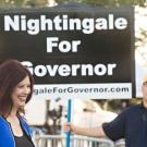 woman in front of sign "Nightingale for Governor" with man holding sign