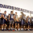 Student-athletes stand under new "UC Davis Health System" sign while Chancellor May talks at podium.