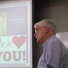 Jonathan Heritage, foreground, with PowerPoint slide behind him, reading "Jonathan Heritage: We Love You."