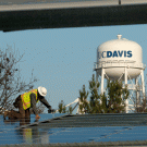 Worker installs solar panels on carportlike structures, in show of UC Davis water tower.