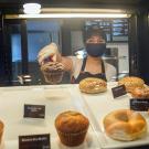 Employee in mask retrieves a pastry from display case.