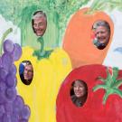 Photo: Four people looking out of a board painted with vegetables