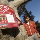 Photo: Student next to tree with red ribbon and a poster