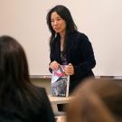 Photo: female teacher addressing her class and holding a physics book