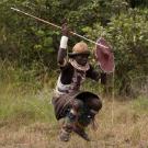 Man in African costume with spear and shield jumping in the air