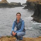 Woman squatting on a cliff's edge at the ocean