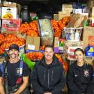 Three firefighters sit in front of a wall of donated items.