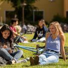 Students sit on the grass in front of a residence hall. 