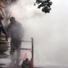 Two workers stand over a grate emitting steam.