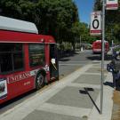 Unitrans bus makes a stop; passenger on sidewalk wears a mask.