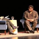 Two men, in chairs, on stage, in conversation.