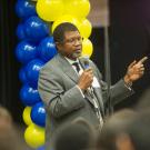 Walter Robinson addresses UC Achieve, with backdrop of blue-and-gold balloons.
