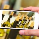 A hand-held cell phone captures an image of wine bottles with corks