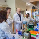 Group of scientists in white lab coats at a bench, smiling amid colorful lab equipment