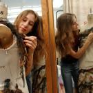 Woman fitting dress forms with textiles in front of double mirror.