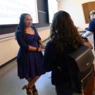 Woman professor talks to students after class with whiteboard in back.