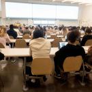 Rear-view photograph of students in a lecture hall facing an instructor.