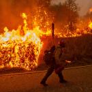 Firefighter walks along highway with flames to his side during Creek Fire response in 2022.