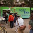 Students line up in front of the bright green AggieEats food truck parking on the side of the Quad.