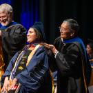 Two faculty in robes hooding smiling graduates at commencement