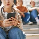 Young girl on cell phone sitting on steps with other youth behind her